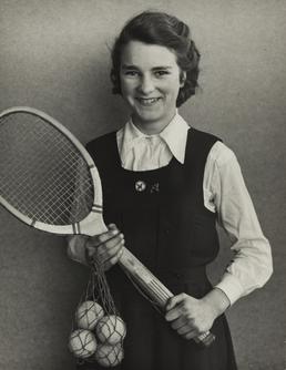 Joan Mayne, standing holding a tennis racquet and…